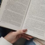 Uppslagen bok som ligger i knäet på en kvinna.