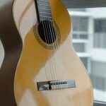 En klassisk gitarr står lutad mot en vägg intill ett fönster