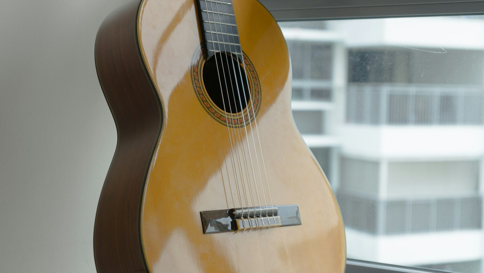 En klassisk gitarr står lutad mot en vägg intill ett fönster