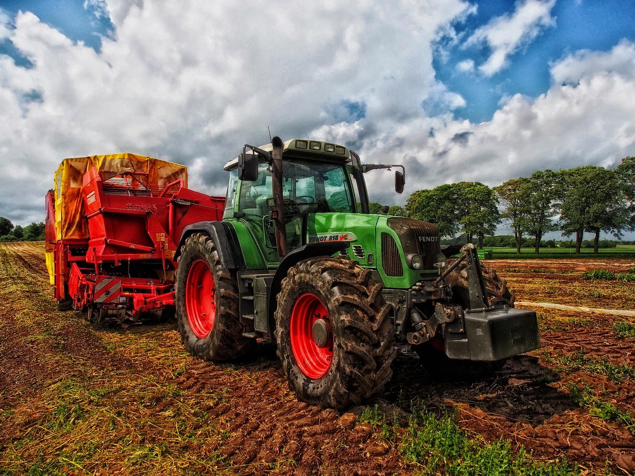 Grön traktor med en röd plog på en åker