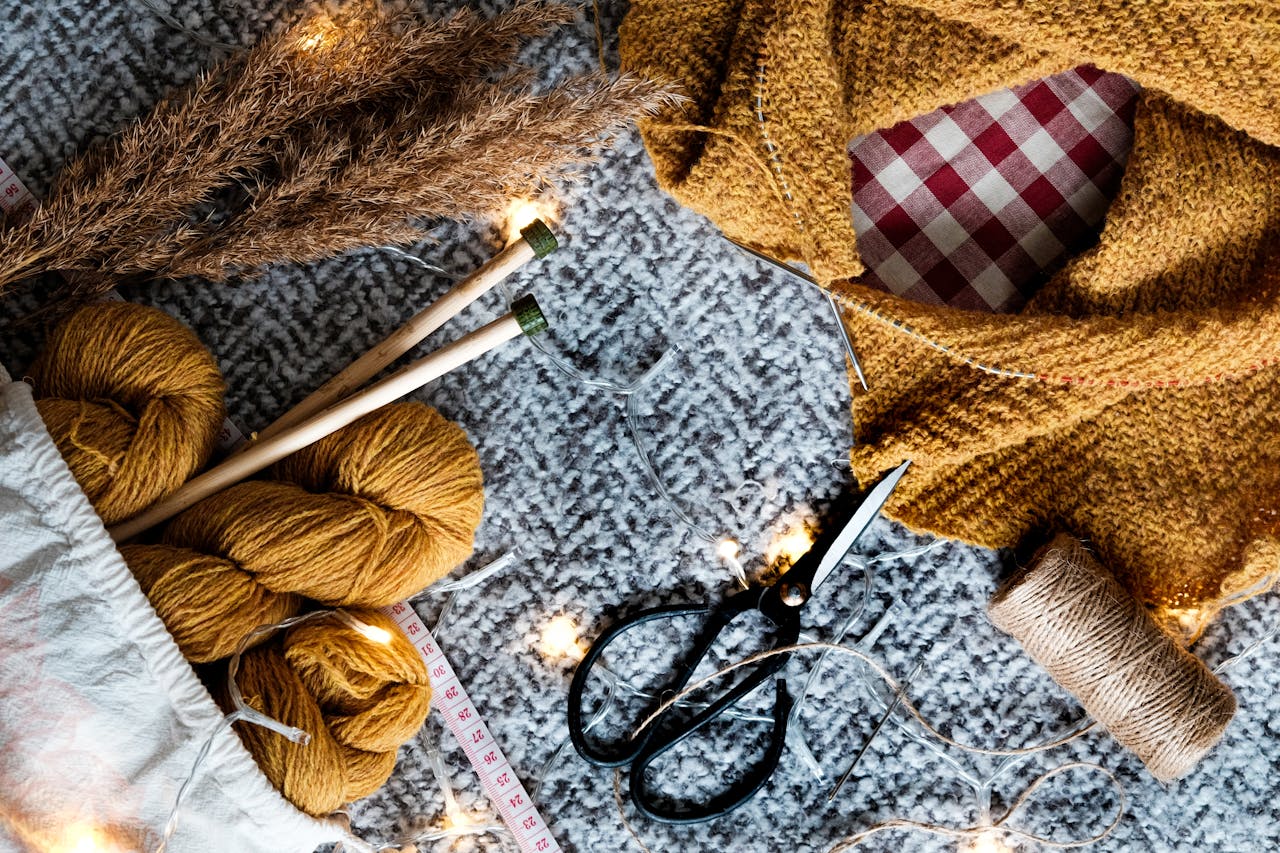 Sax, garn och stickor mot grå och röd-vitrutig bakgrund