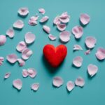 Ett mjukt rött hjärta i mitten och rosa blomblad runtomkring ligger på en himmelsblå bakgrund.