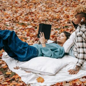 Två läsande personer på en filt omgiven av höstlöv