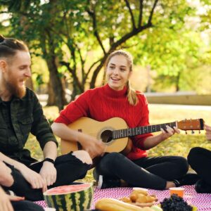 Fyra personer som sitter tillsammans på en filt utomhus, en spelar gitarr.