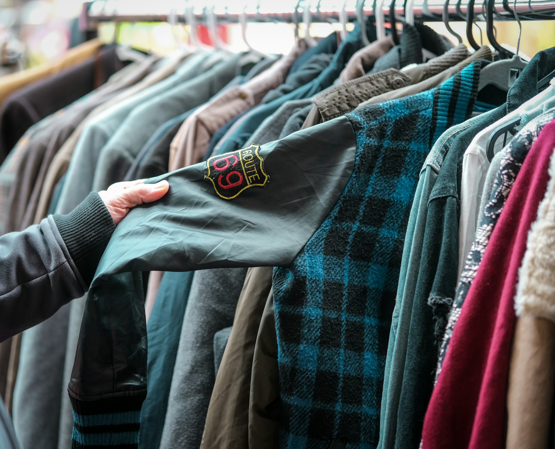 Hängande kläder på galgar (second hand) och en person som känner på en jacka.