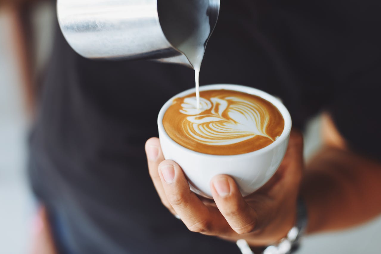 En barrista som skapar ett vackert mönster med mjölkskum i en kaffekopp.