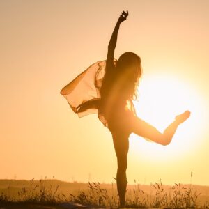 Siluetten av en kvinna som dansar med en sjal framför en lågt stående sol.