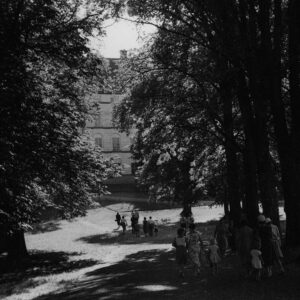Äldre svartvit bild på Engelska parken i Uppsala. En stig som sommarklädda människor går på. Stora träd på sidorna och ett gammalt hus i bakgrunden.