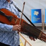 Bild på person i skjorta som spelar nyckelharpa.