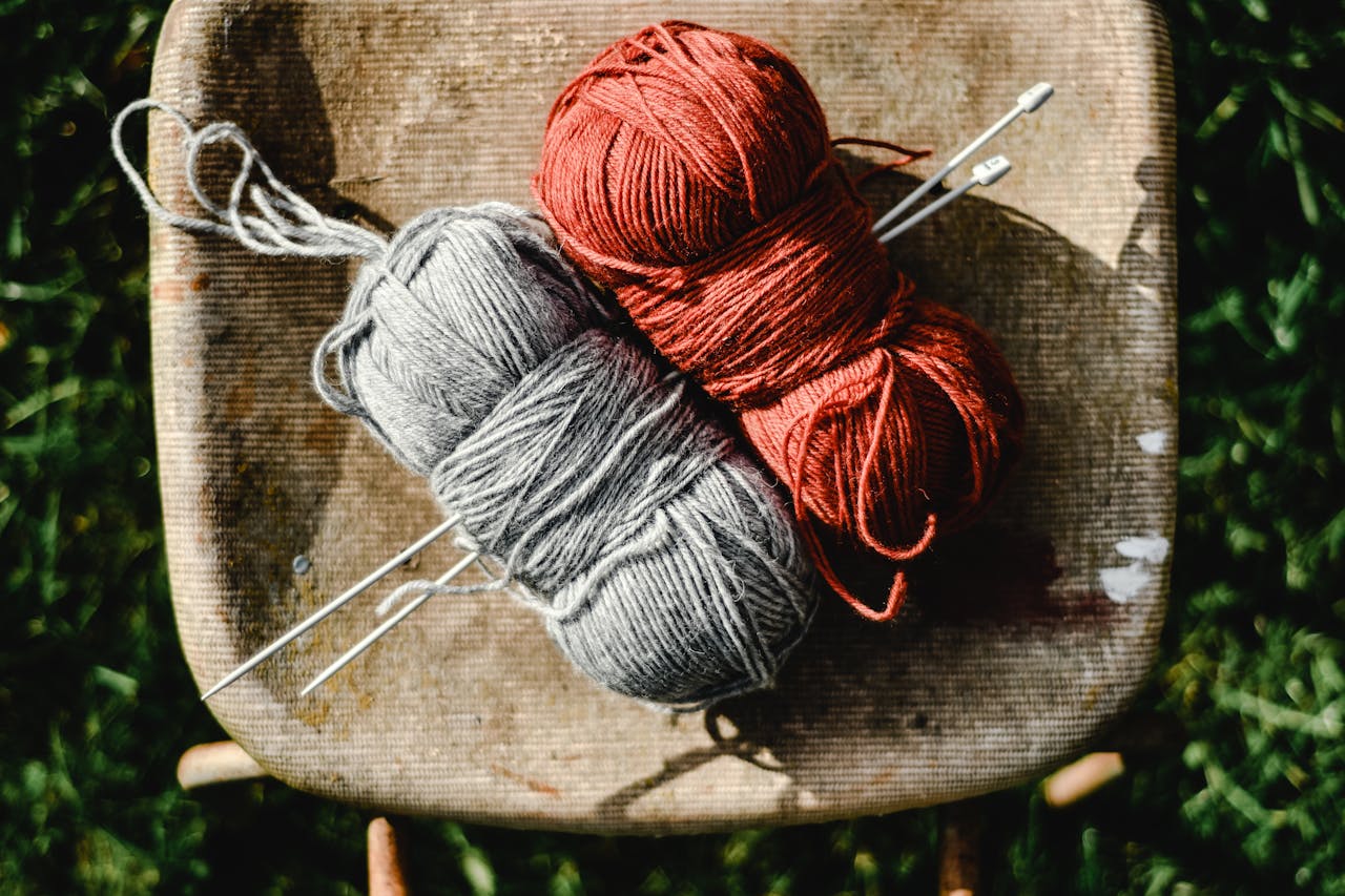 Bild på två garn i rött och grått med stickor.