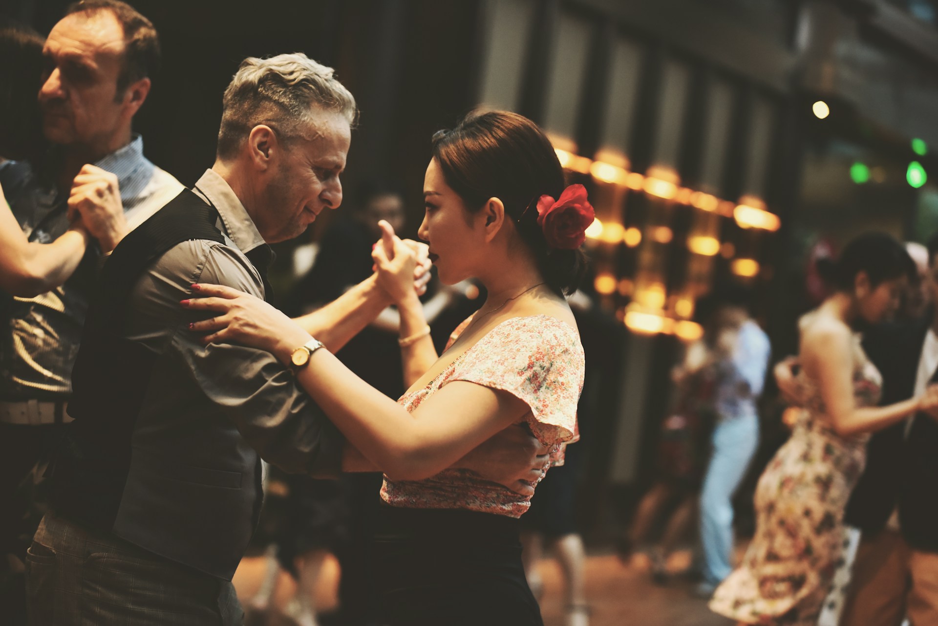 Två personer dansar en pardans med andra dansande par i bakgrunden.
