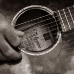 Närbild på en guitar med fokus på gitarrspelande hand