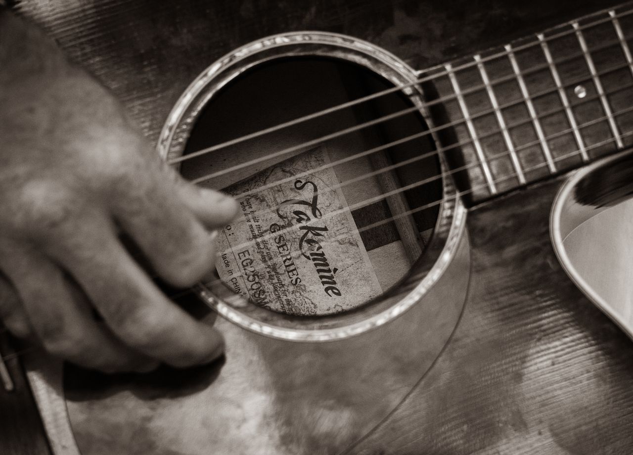 Närbild på en guitar med fokus på gitarrspelande hand