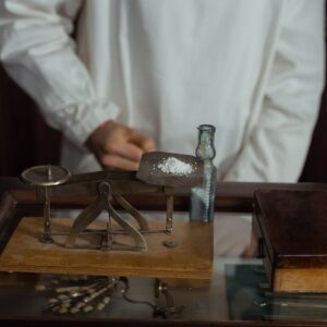 Bilden visar en person i en historisk apoteksmiljö som arbetar med traditionell läkemedelstillverkning.