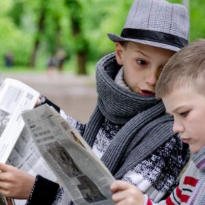 Två barn som håller i varsin tidning utomhus.