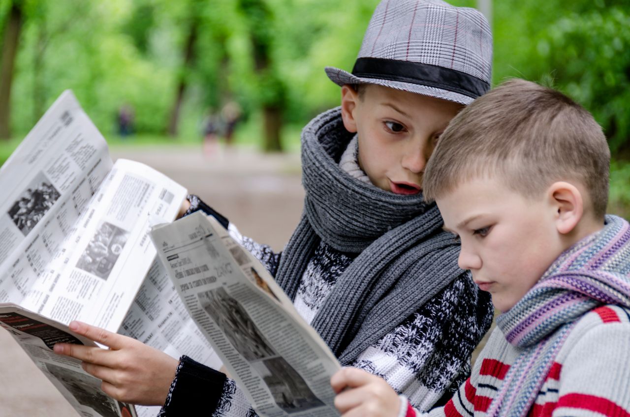 Två barn som håller i varsin tidning utomhus.