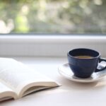 Bild på en öppen bok och en kaffekopp bredvid på ett bord.