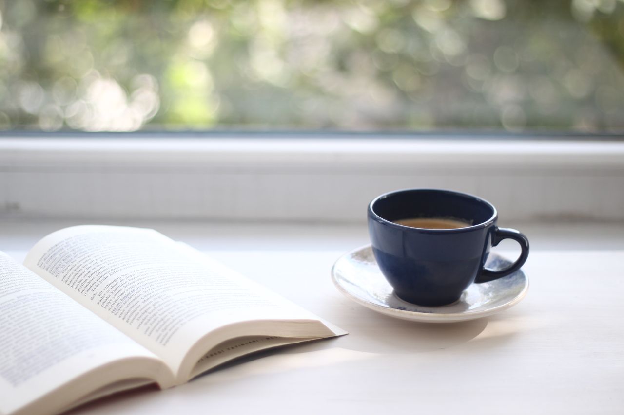 Bild på en öppen bok och en kaffekopp bredvid på ett bord.