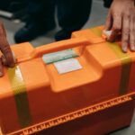Närbild av händer som håller en orange nödsituation medicinsk kit inomhus.