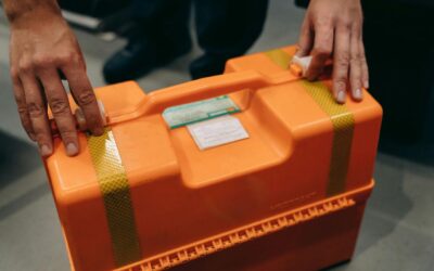 Närbild av händer som håller en orange nödsituation medicinsk kit inomhus.
