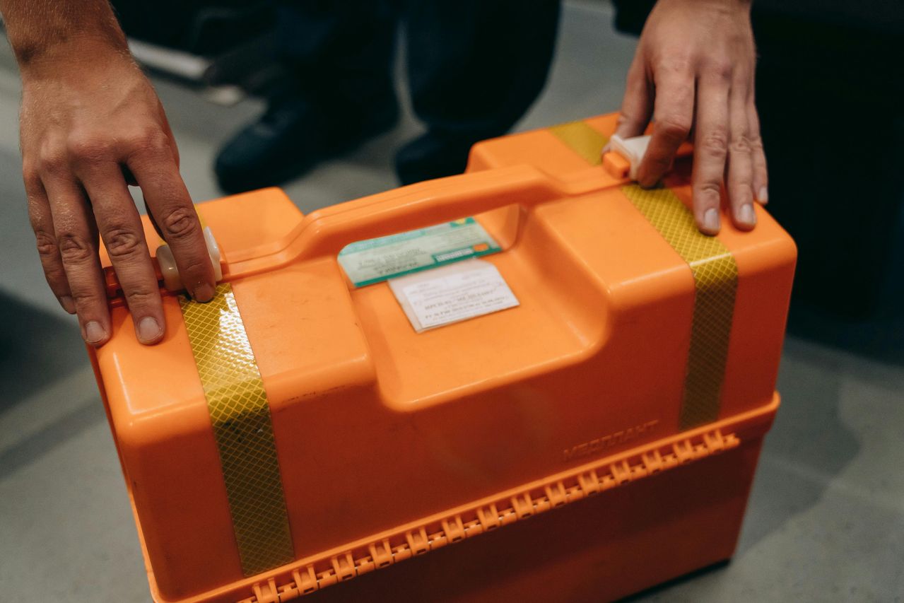 Närbild av händer som håller en orange nödsituation medicinsk kit inomhus.