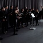 En kör som övar under en dirigents ledning i en inomhusstudio.