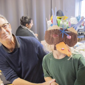 Bild på en vuxen som sitter bredvid ett barn som har en mask på sig.