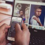 Bilden visar en dataskärm med bilder på skärmen. en person håller i en mobiltelefon där handen syns i bilden.