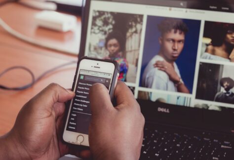 Bilden visar en dataskärm med bilder på skärmen. en person håller i en mobiltelefon där handen syns i bilden.