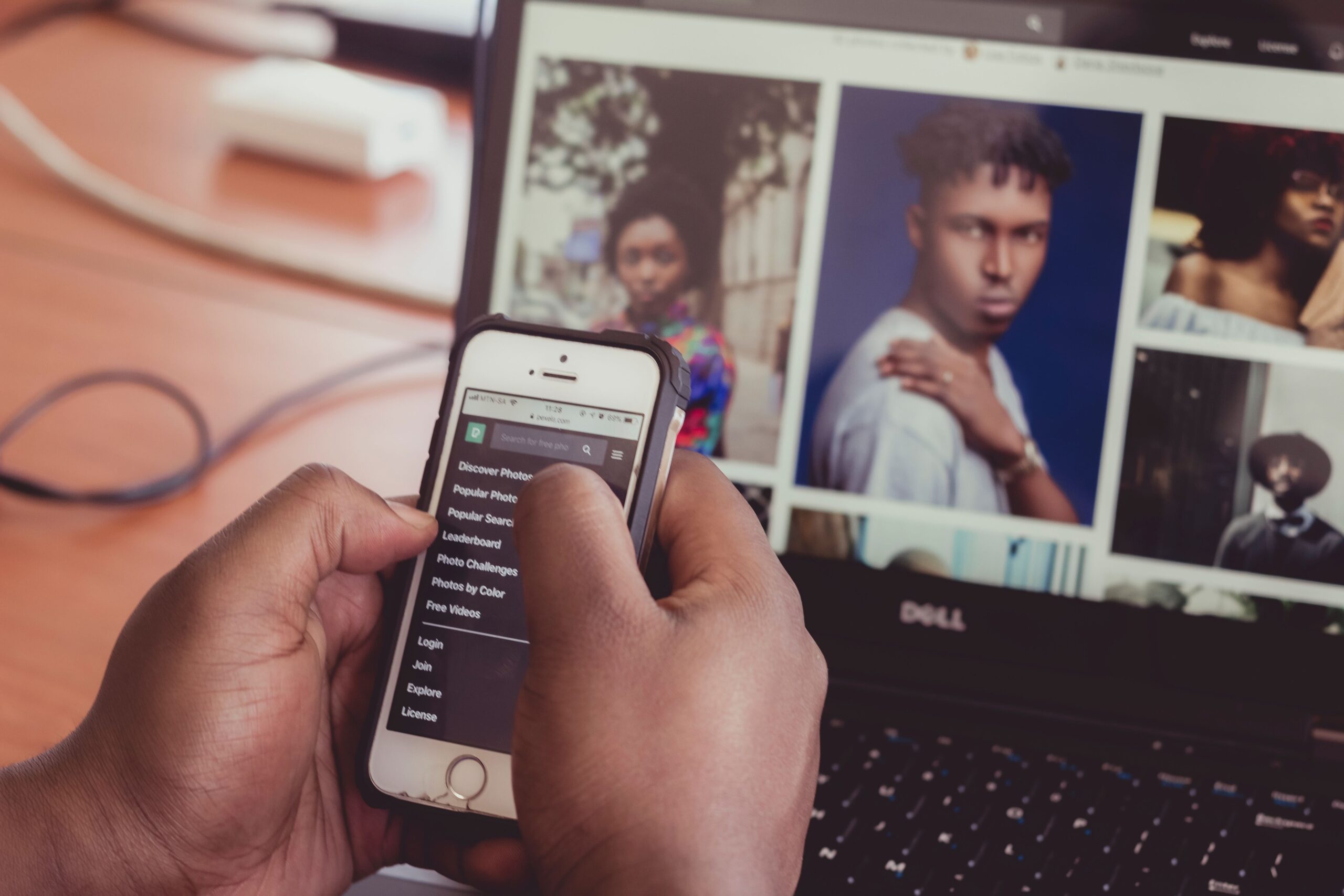 Bilden visar en dataskärm med bilder på skärmen. en person håller i en mobiltelefon där handen syns i bilden.