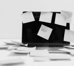 Bild på en dator som har massa post-it-lappar på sig, en där det står "Help" på.