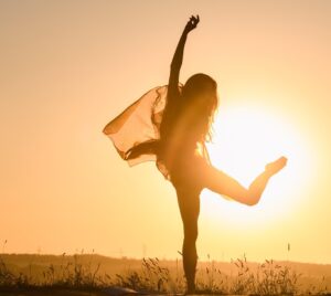Siluetten av en kvinna som dansar med en sjal framför en lågt stående sol.